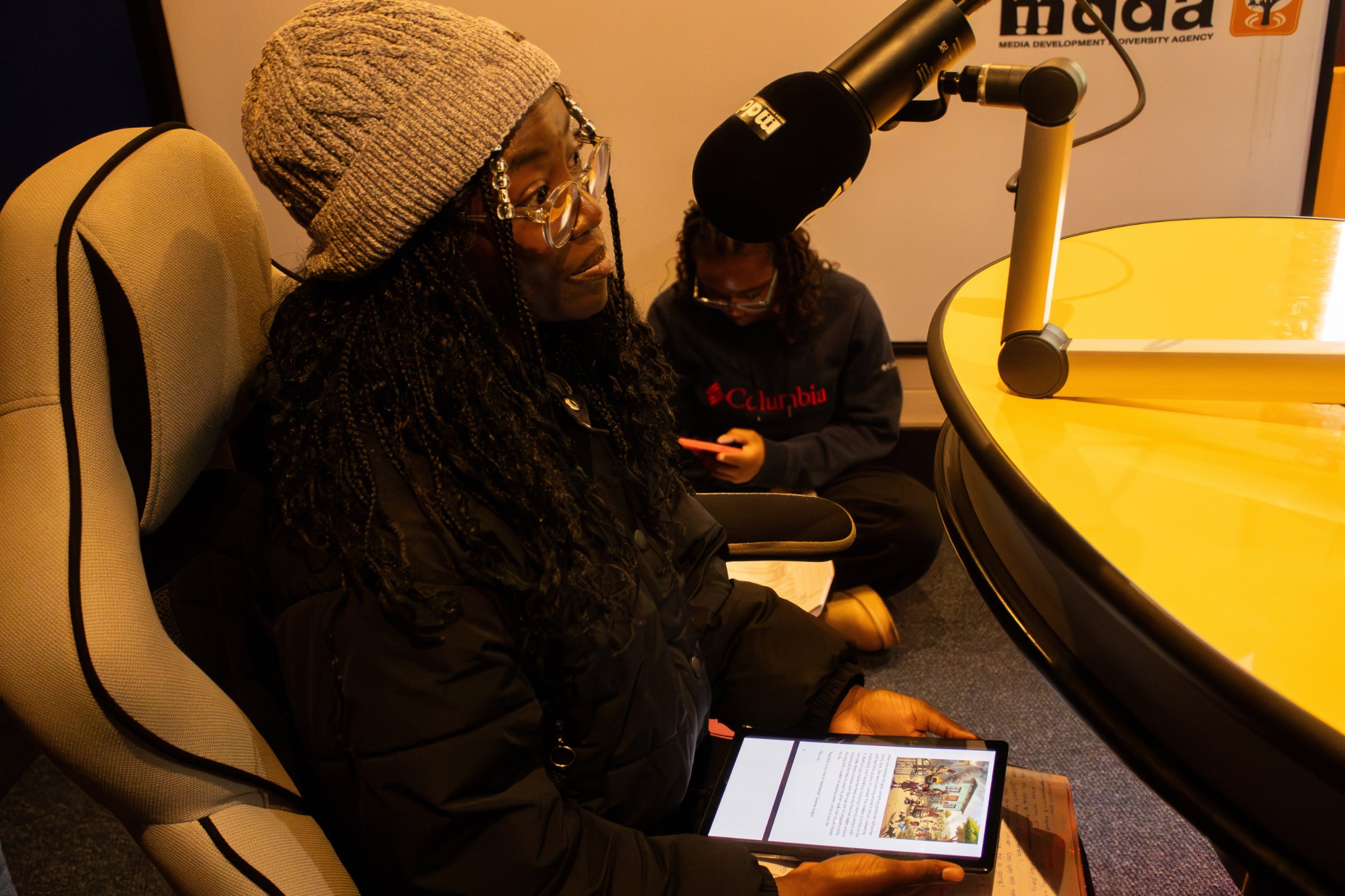 Funo Masindi, creator of Adventures with Sesona, reading from a tablet at the mic