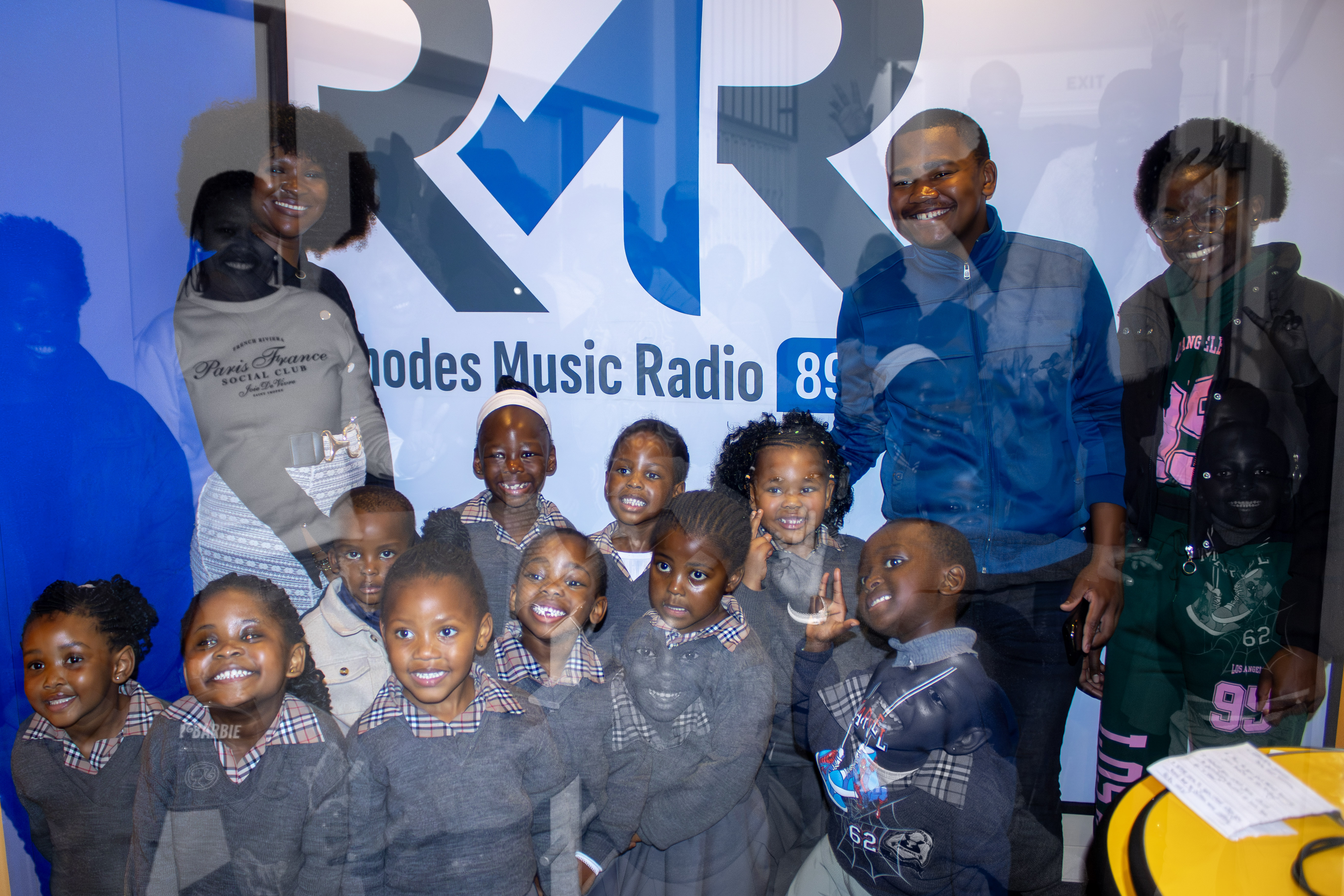 A group of Playmates and the team smiling in front of the Rhodes Music Radio logo